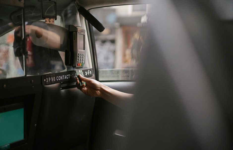 Unrecognizable person sitting in taxi car and paying by credit card and payment terminal in daytime