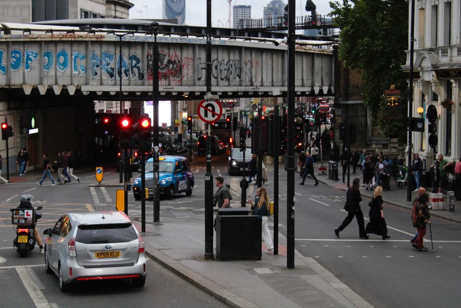 London street scene with traffic, pedestrians, and graffiti-covered bridge.